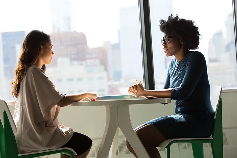 A business person interviews an applicant at a table in front of a large window.