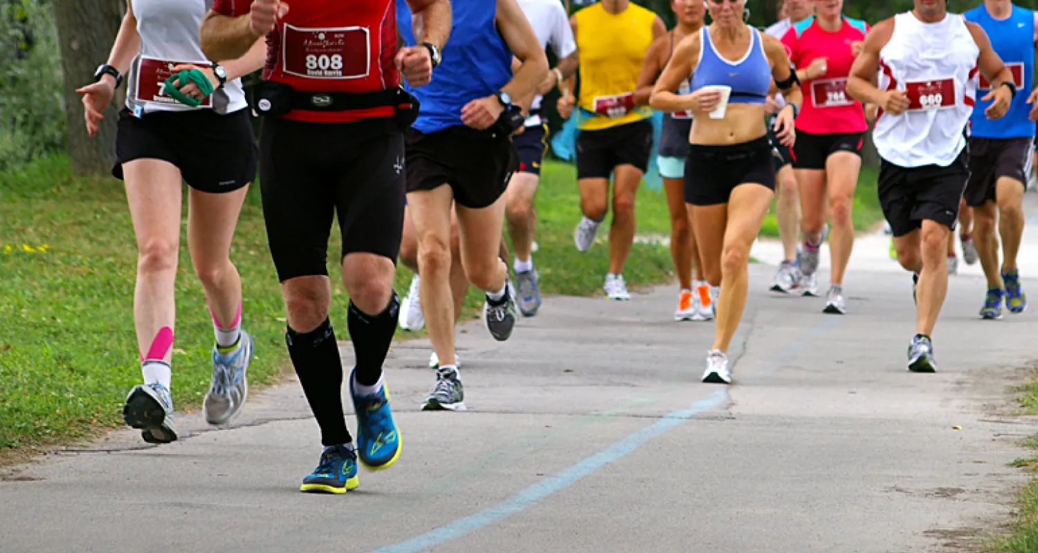 Photo of people running in a large group on a lines path, surrounded by grass and trees.