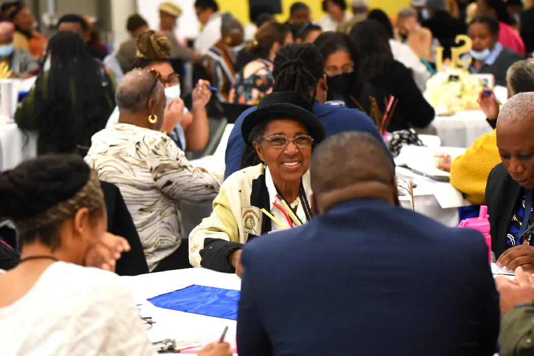 Groups of African Americans sit together at round tables, talking and engaging with one another.