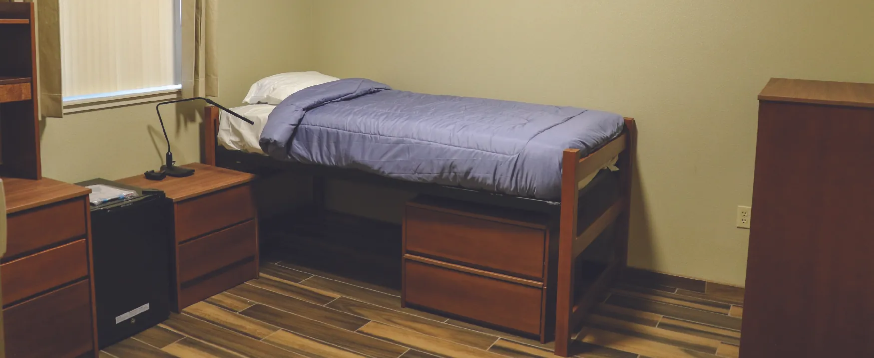 A photograph shows a dorm room with a bed and matching furniture.