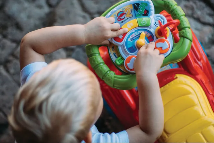Image of child playing with a steering wheel full of buttons, knobs, and turn dials on a child’s ride on car.