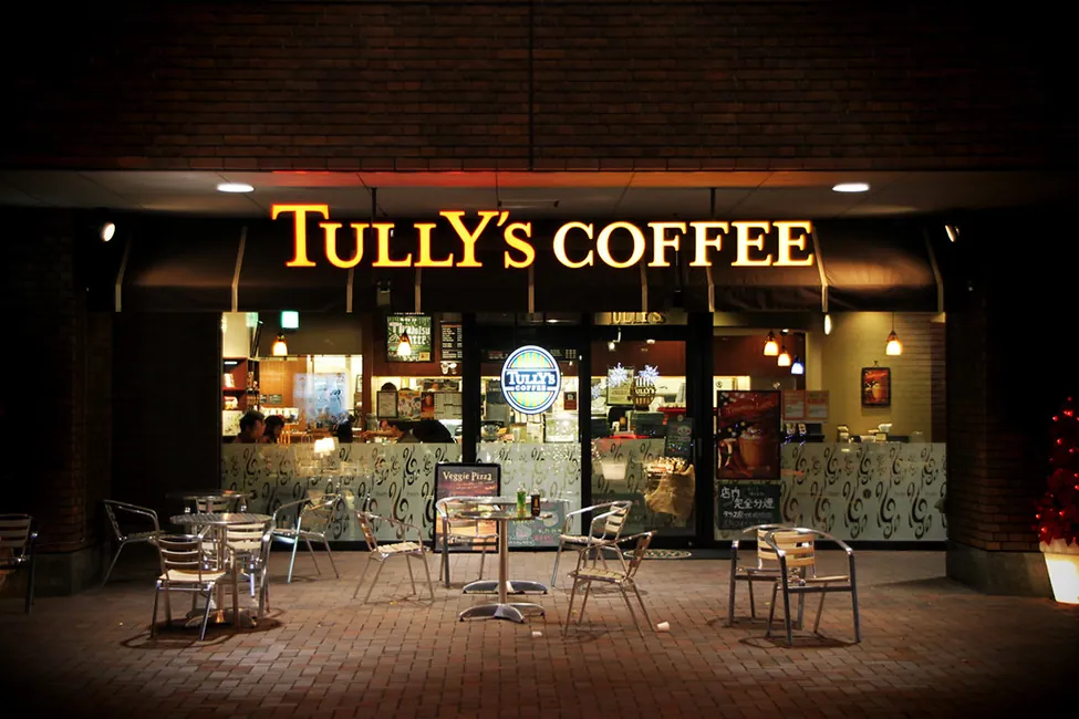 An outside view of a coffee shop. People are seen inside sitting and drinking coffee.