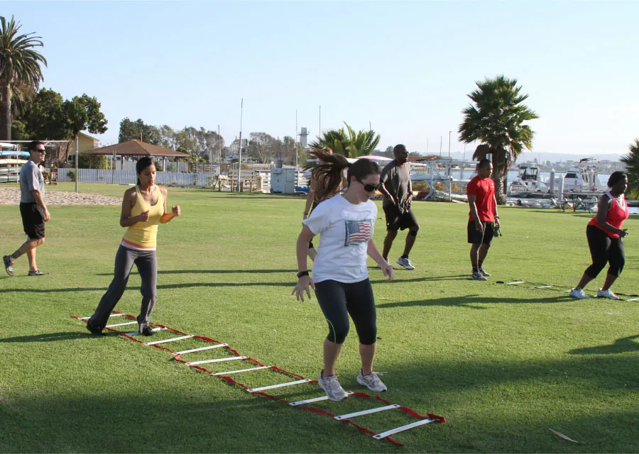 Photo of individuals outside practicing slaloms on a rope ladder on the ground.