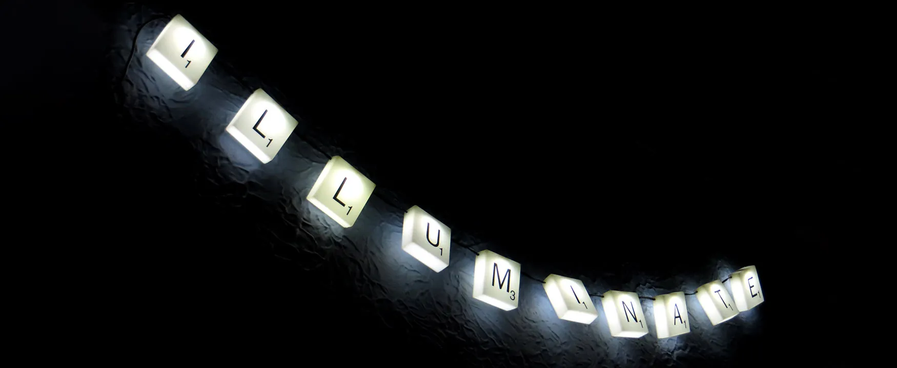 An image tiles held together with string, with characters written on tiles, reading "Illuminate"