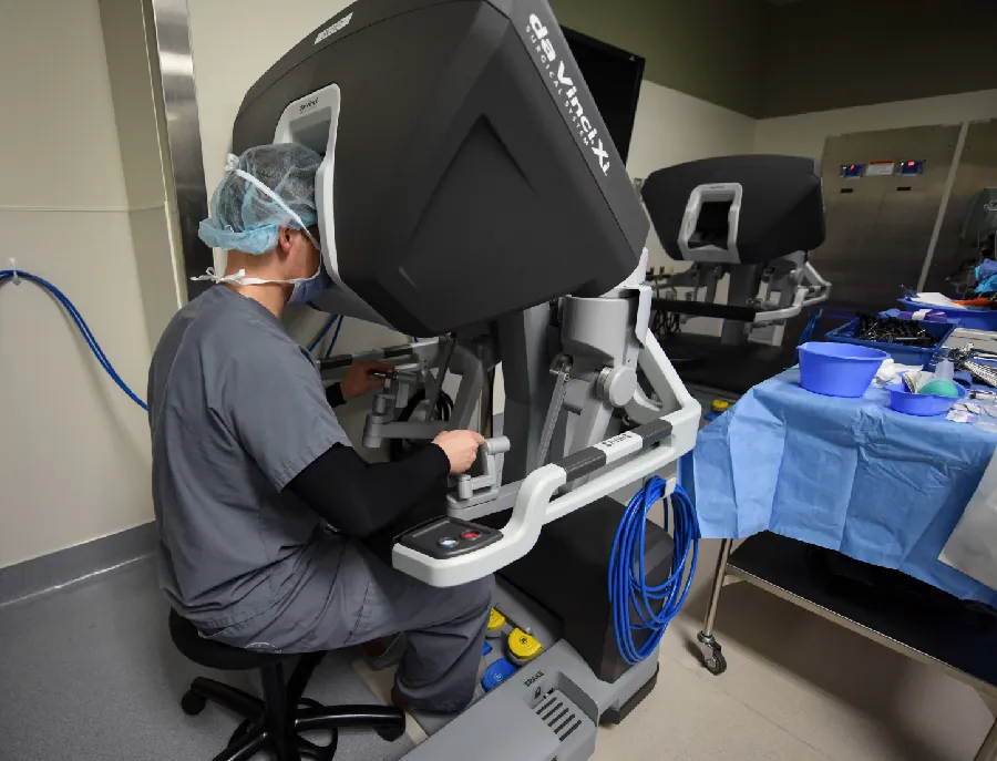 Photo of healthcare worker sitting at a robotic machine in a medical setting.