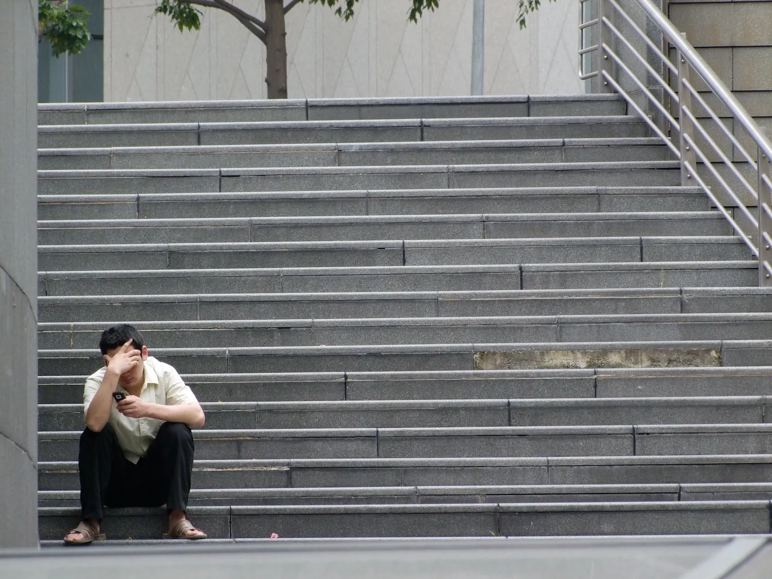 A person sits on the bottom of a staircase with their hand on their head.