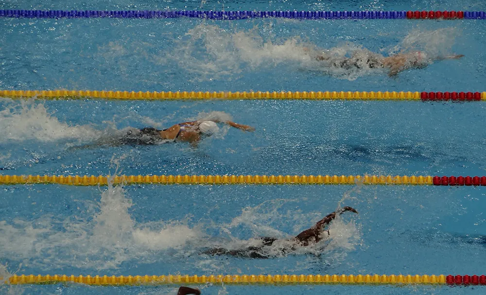 Three swimmers are racing in separate lanes in a swimming pool. The swimmer in the top lane is in first place, the swimmer in the bottom lane is in second place, and the swimmer in the middle lane is in third place.