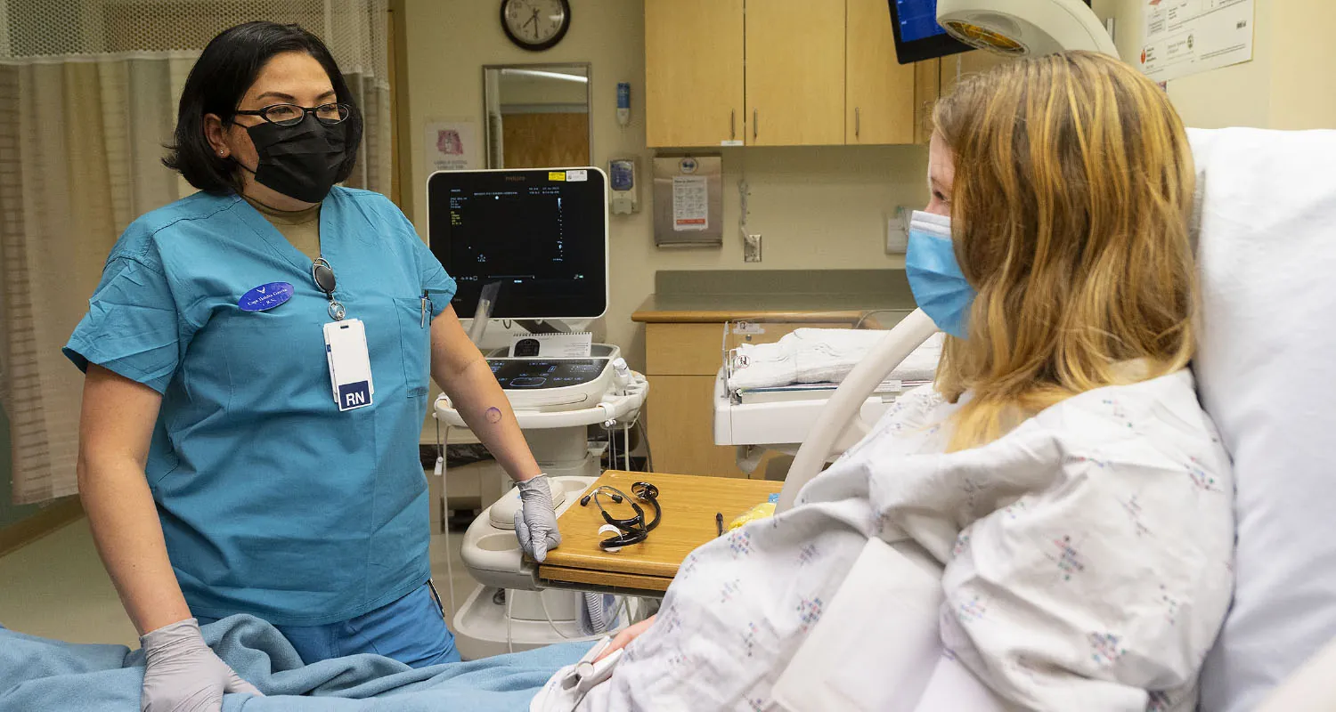 Patient in hospital bed with nurse standing beside.