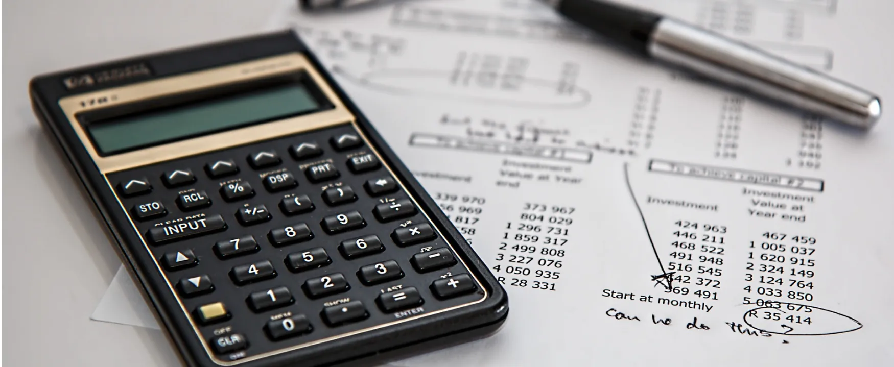 A calculator sits on a sheet of paper.  On the paper are investment and return amounts, with a handwritten note that asks, “Can we do this?”