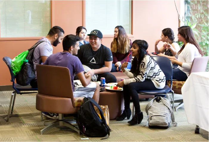 Photo of group of individuals sitting on chairs around tables talking to each other.
