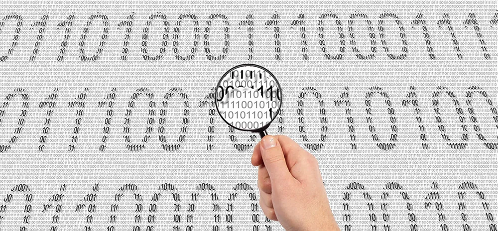 A person holding a magnifying glass is observing binary code.