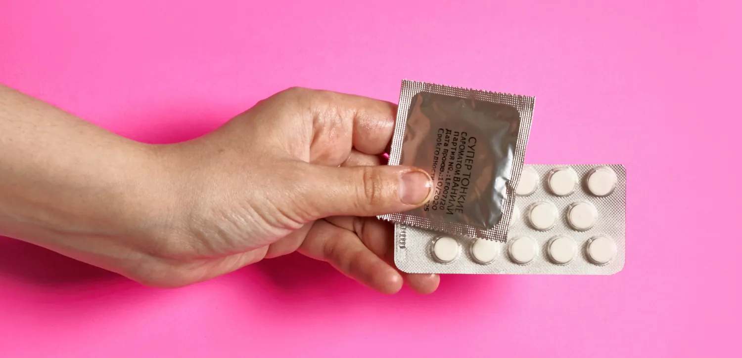 Photo of hand holding contraceptive pills and a condom.