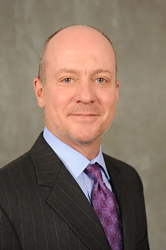 A person wearing a suit and tie smiles for a portrait.