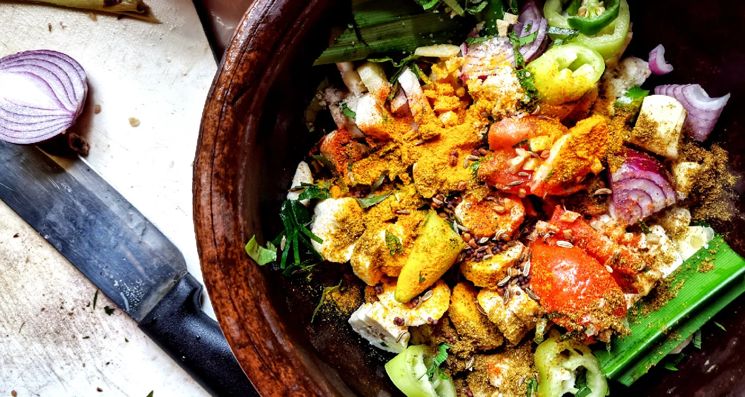 A wooden bowl contains chopped, raw vegetables that are covered in spices.