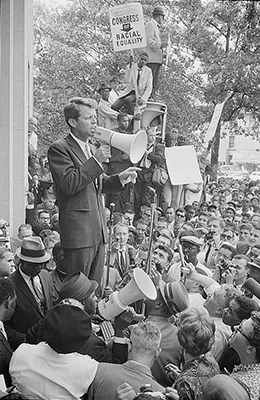 A photograph shows Robert Kennedy speaking to a large crowd through a megaphone.