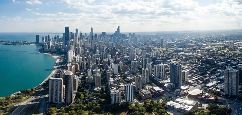 An aerial photograph of the Chicago skyline shows tall skyscrapers along a body of water. The tallest buildings are concentrated toward the back of the photo; while smaller buildings appear on the right side of the photograph.