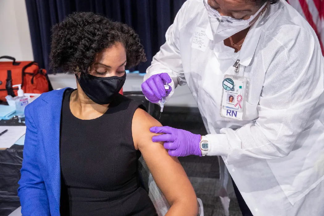 A nurse sticks a needle into the upper arm area of a person sitting in a chair.