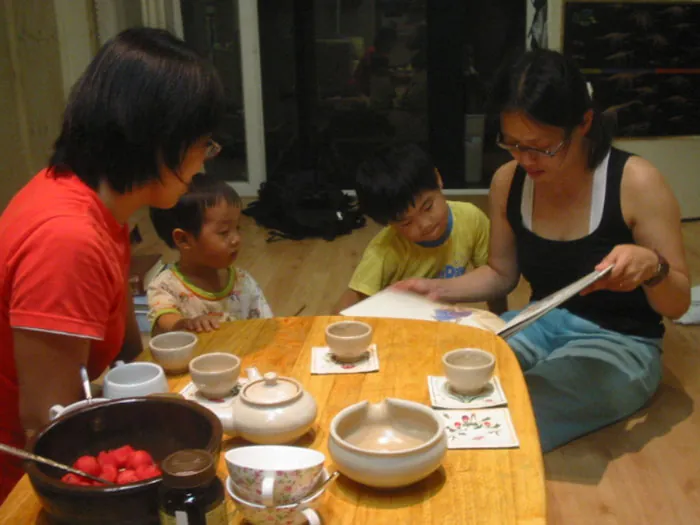 Photo of two adults and two children sitting on the floor at a low table reading a book together.