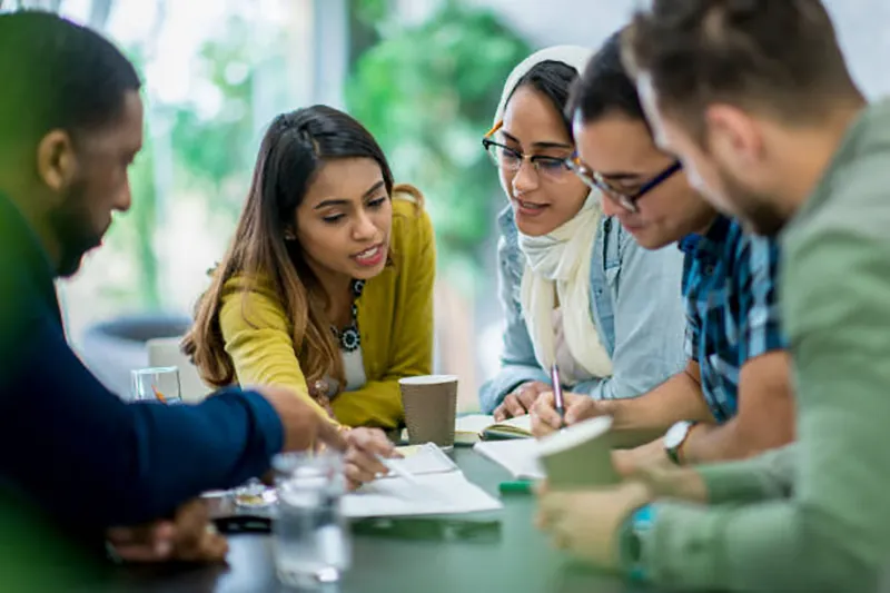 Five students gather closely around a table to review a document.