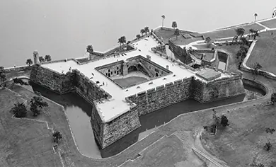 An aerial photograph shows the Spanish fort of Castillo de San Marcos, a square, high-walled structure facing the water and including a surrounding moat.