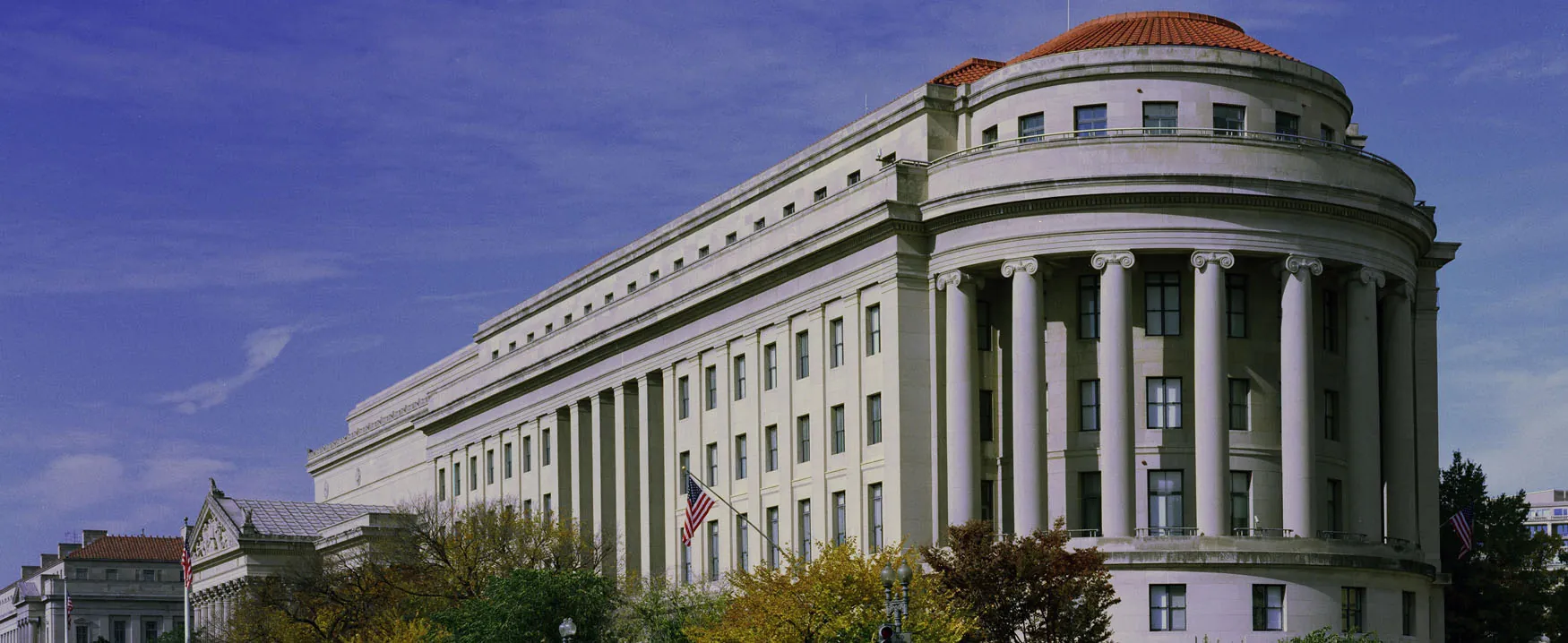 A picture of the United States Federal Trade Commission building in Washington DC.  The seven-story building is made of gray-white granite.  One end of the building is rounded with large pillars.  The rest of the building is rectangular.