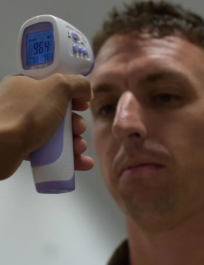 A medical worker holds a temporal thermometer in front of a patient’s forehead