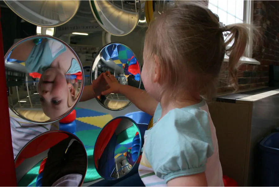 Photo of toddler seeing their image reflected in a mirror.