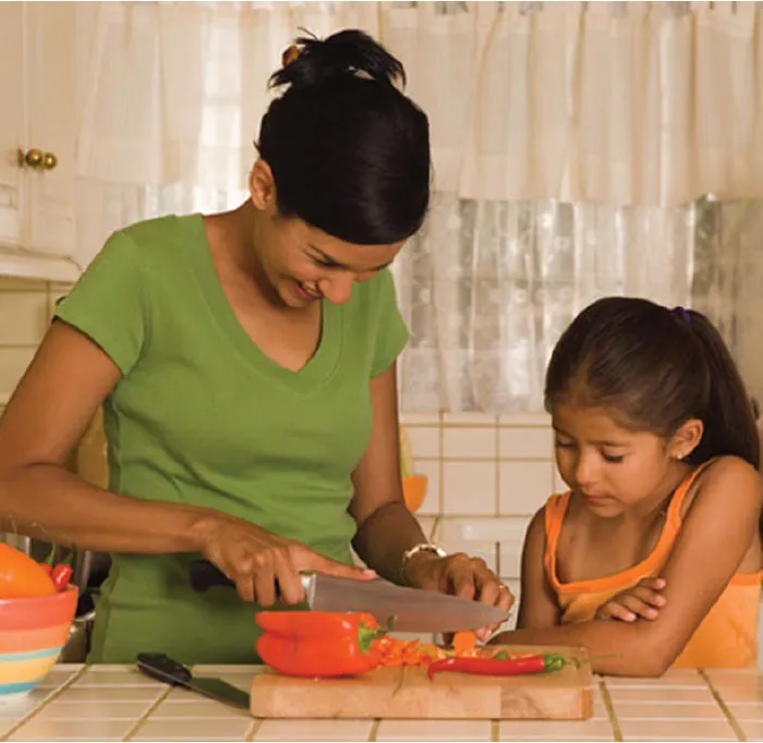 Photo of child watching adult cut food items at a kitchen counter.