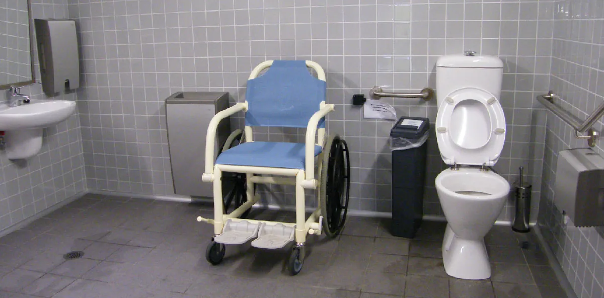 Photo of a pool access chair in a large, accessible bathroom with handrails and lowered sink.