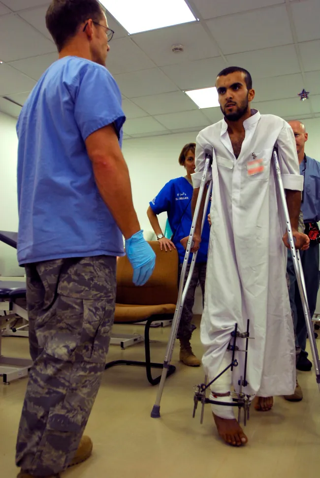 Individual on crutches and pins in their leg walks toward a healthcare worker while two other people look on.