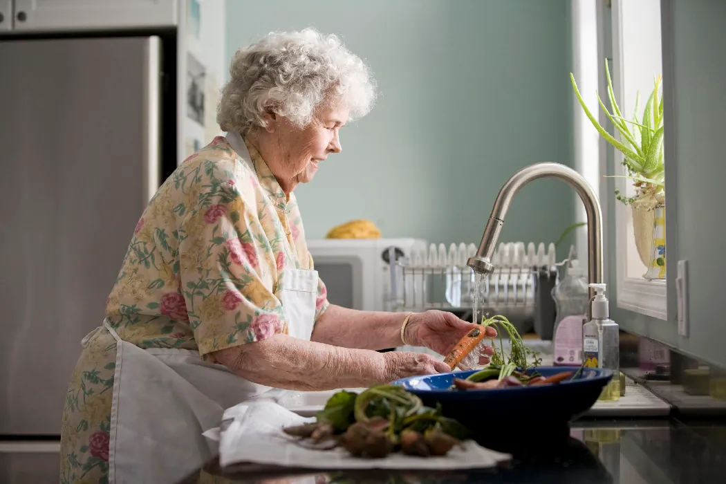 An older person washes vegetables in their kitchen.