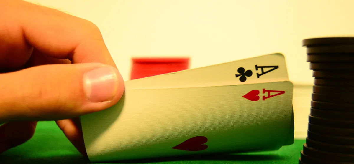 Close up of a hand lifting two playing cards at a poker table.