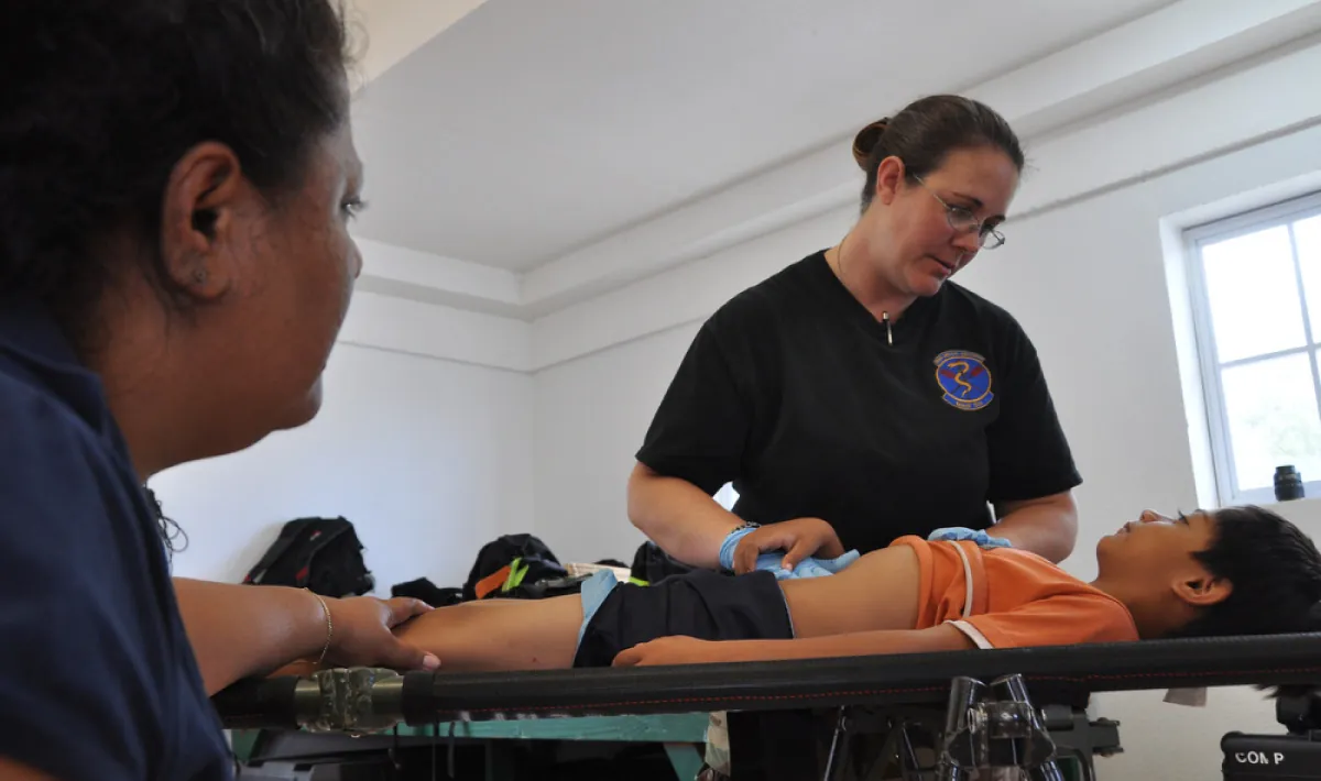 A color photograph shows two nurses performing an abdomen check on a young child.