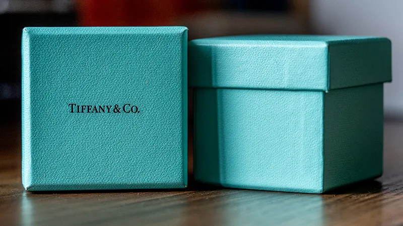 Two small blue Tiffany’s boxes are next to each other on a table. The box on the left is turned on it’s side so the “Tiffany & Co.” label is visible.