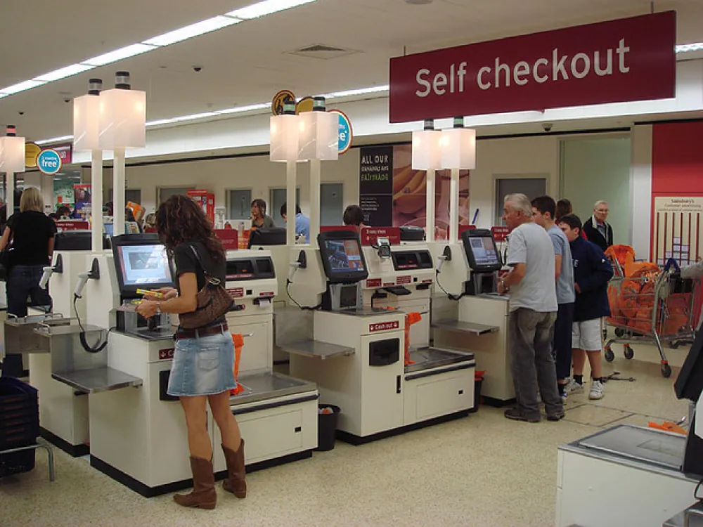 Photo of individuals using self-checkout lanes at a store.