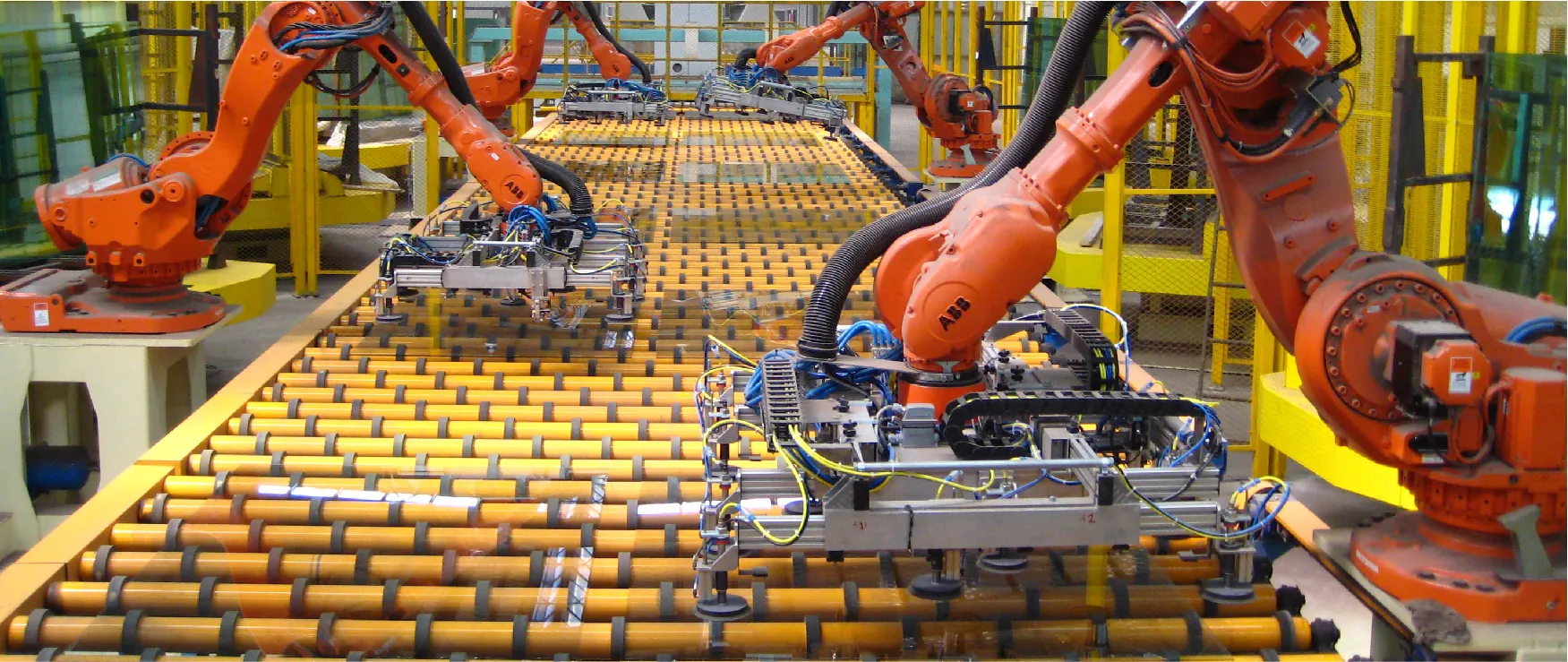 Robot arms loading an unloading sheets of float glass from a rolling conveyor belt.