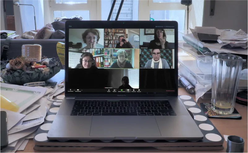 A laptop screen shows seven windows with people’s faces in various locations.