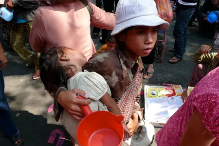 A young, impoverished boy is shown holding a baby girl. 