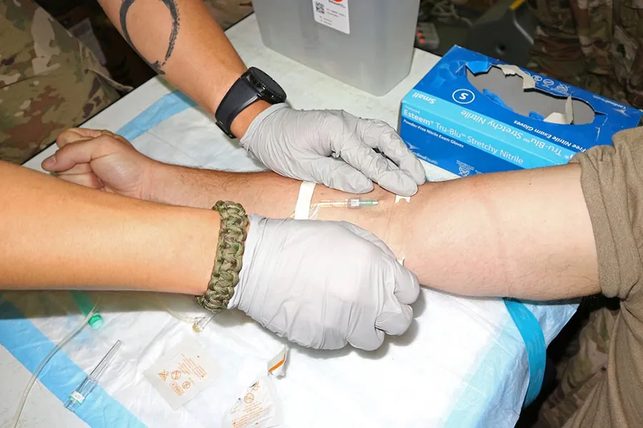 A person applies transparent dressing to cover the catheter on a person's arm, serving as the entry point for a line. The catheter and surrounding tissue are clearly visible through the dressing.