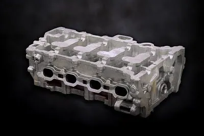 An engine cylinder head, which appears as a curved rectangular structure with four large openings and a number of attachment points for other components. The substructures, angles, and details reveal a complex interior structure.