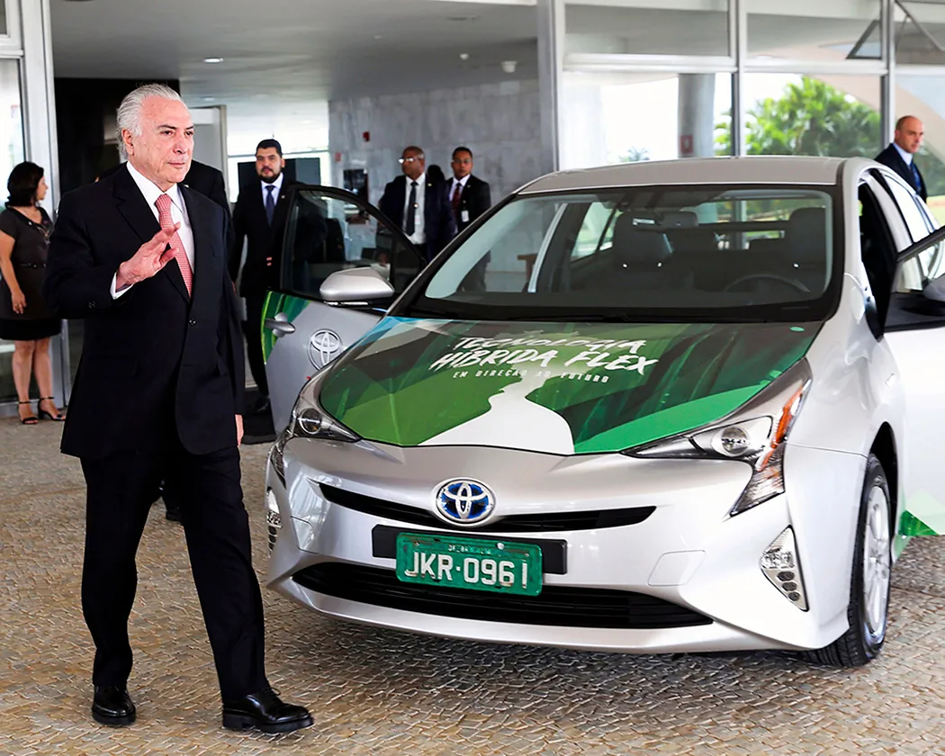 A photo shows Michel Temer waving to the camera as he stands next to a Toyota Prius hybrid electric vehicle at the launch ceremony of the world's first flex hybrid vehicle.