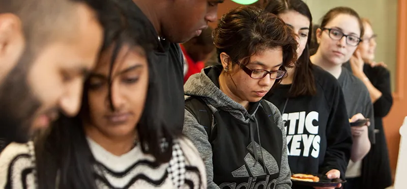 A group of students is standing in a line holding plates of food.