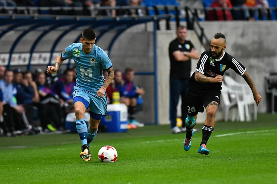 Soccer players are shown on a field and one of them is about to kick the ball.