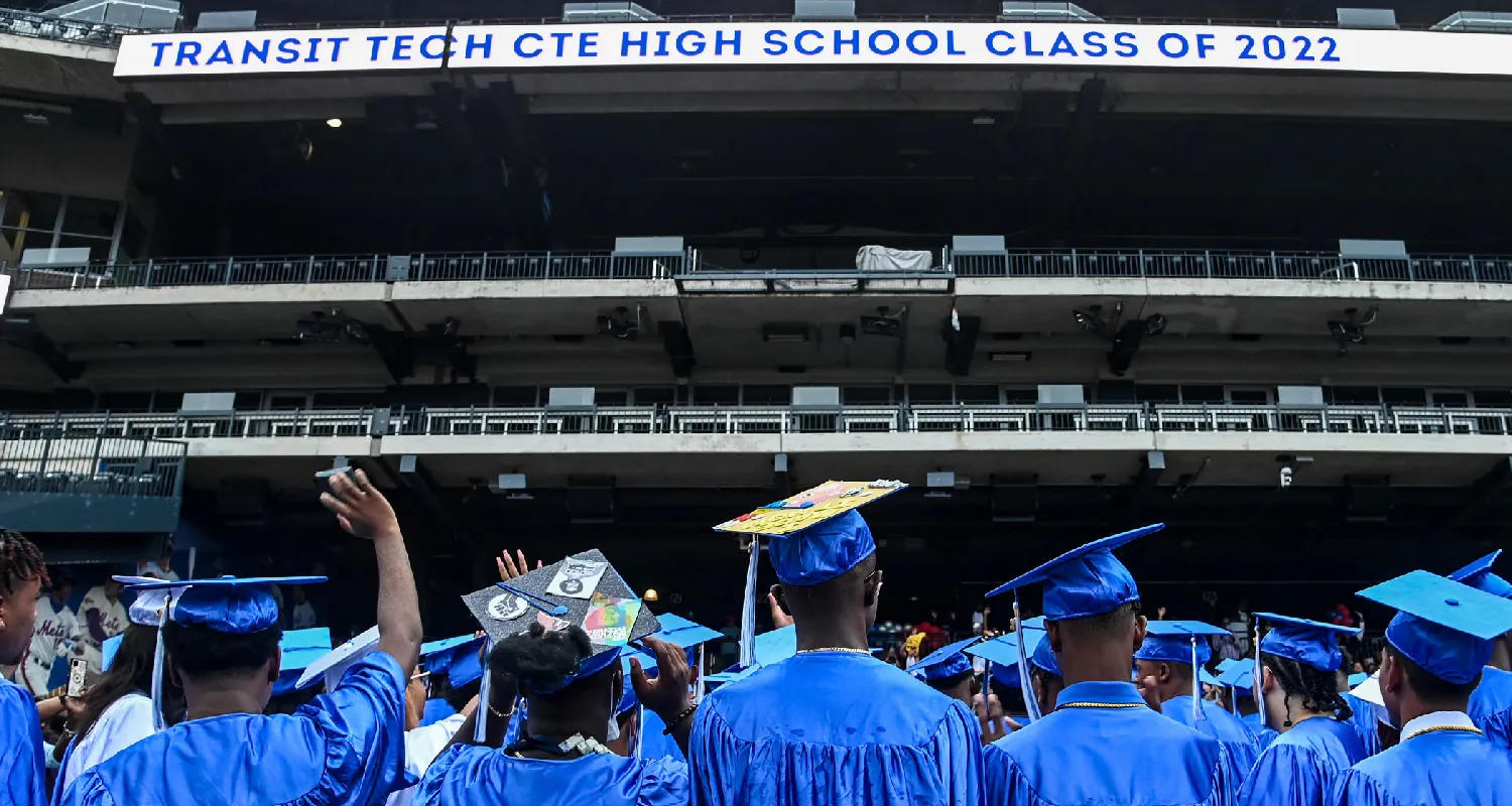 A photo shows students wearing graduation caps and gowns from behind. Some are waving and some have the top of their cap decorated. A sign above them says Transit Tech CTE High School Class of 2022.