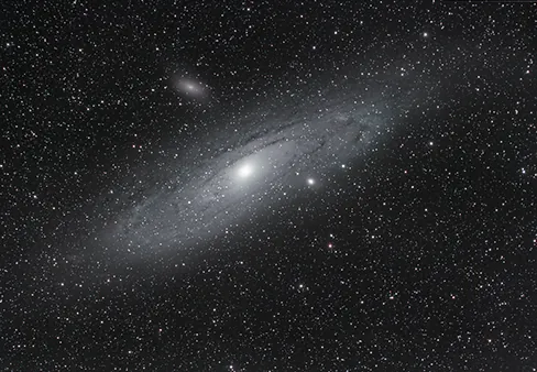 The majestic Andromeda Galaxy (M31), our closest large galactic neighbor, with its faint spiral arms and bright core, surrounded by a myriad of stars in the vast cosmic expanse. Two smaller companion galaxies are also visible near M31.