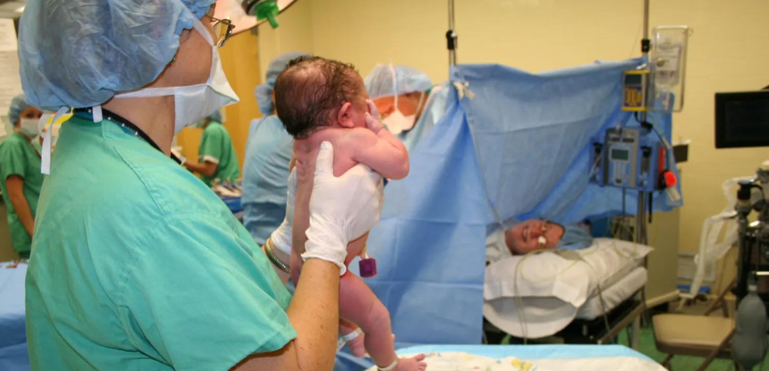 A nurse displays a newborn baby in an operating room.