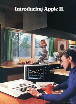 An advertisement shows a young man seated at a kitchen table working on a 1970s-style computer. A woman, who is preparing food at the kitchen counter, looks over her shoulder at him and smiles.