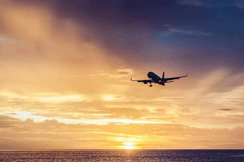 An airplane flies over a body of water while the sun is setting.