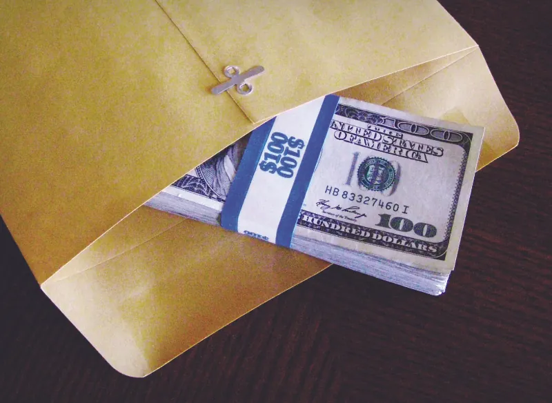 This image shows a stack of 100 dollar bills half in a clasp envelope.