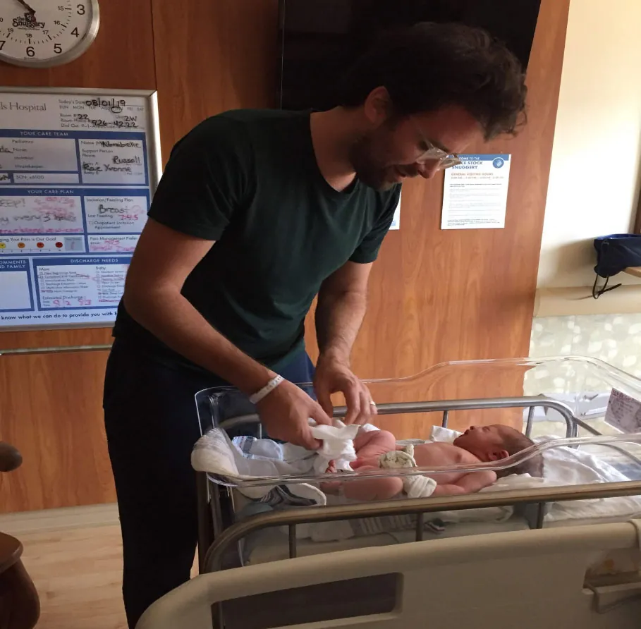Photo of a father changing a baby’s diaper in the hospital bassinet.